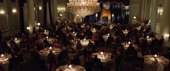 Movie still from “The Young and Prodigious T.S. Spivet” (2013), directed by Jean-Pierre Jeunet – A group of people sitting at tables in front of a microphone; Extreme Wide shot, High angle
