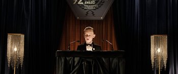 Movie still from “The Young and Prodigious T.S. Spivet” (2013), directed by Jean-Pierre Jeunet – A boy in a tuxedo is giving a speech at a podium; Medium shot, Low angle
