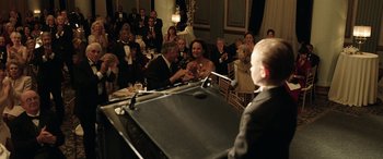 Movie still from “The Young and Prodigious T.S. Spivet” (2013), directed by Jean-Pierre Jeunet – A man standing at a piano in front of an audience; Medium shot, Over the shoulder angle