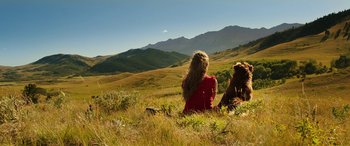 Movie still from “The Young and Prodigious T.S. Spivet” (2013), directed by Jean-Pierre Jeunet – A woman sitting in the grass with a bear; Wide shot, High angle