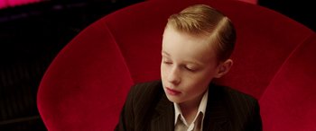 Movie still from “The Young and Prodigious T.S. Spivet” (2013), directed by Jean-Pierre Jeunet – A boy in a suit sitting on a red chair; Close Up shot, High angle