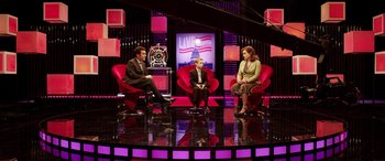 Movie still from “The Young and Prodigious T.S. Spivet” (2013), directed by Jean-Pierre Jeunet – Two women and a man sitting on red chairs on a stage; Wide shot, High angle