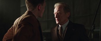Movie still from “Their Finest” (2016), directed by Lone Scherfig – A man in a suit and tie talking to another man in a suit and tie; Close Up shot, Over the shoulder angle