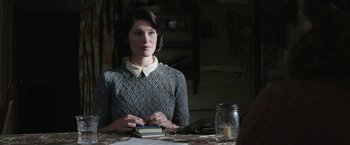 Movie still from “Their Finest” (2016), directed by Lone Scherfig – A woman sitting at a table holding a book; Medium shot, Over the shoulder angle
