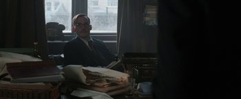Movie still from “Their Finest” (2016), directed by Lone Scherfig – A man sitting at a desk in front of a window; Medium shot, Over the shoulder angle