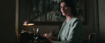 Movie still from “Their Finest” (2016), directed by Lone Scherfig – A woman sitting at a table in front of a painting; Medium shot, Low angle