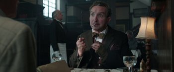 Movie still from “Their Finest” (2016), directed by Lone Scherfig – A man sitting at a table smoking a cigarette; Close Up shot, Over the shoulder angle