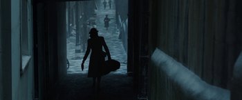 Movie still from “Their Finest” (2016), directed by Lone Scherfig – A woman walking down a street holding a skateboard; Wide shot, Over the shoulder angle