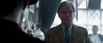 Movie still from “Their Finest” (2016), directed by Lone Scherfig – An older man wearing a suit and tie in front of a window; Close Up shot, Over the shoulder angle
