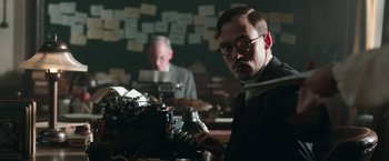 Movie still from “Their Finest” (2016), directed by Lone Scherfig – A man in a room with papers on the wall behind him; Medium shot, Low angle