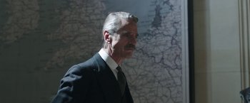 Movie still from “Their Finest” (2016), directed by Lone Scherfig – An older man wearing a suit and tie; Close Up shot, Over the shoulder angle