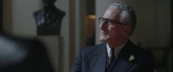 Movie still from “Their Finest” (2016), directed by Lone Scherfig – An older man wearing a suit and glasses; Close Up shot, Over the shoulder angle