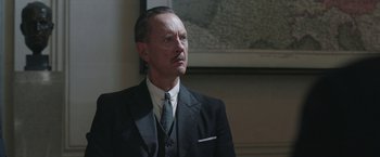 Movie still from “Their Finest” (2016), directed by Lone Scherfig – A man in a suit and tie looking to his left; Close Up shot, Low angle