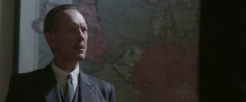 Movie still from “Their Finest” (2016), directed by Lone Scherfig – An older man in a suit standing in front of a map; Close Up shot, Low angle
