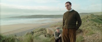 Movie still from “Their Finest” (2016), directed by Lone Scherfig – A man and a woman standing on top of a grass covered hill; Medium shot, Low angle