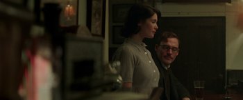 Movie still from “Their Finest” (2016), directed by Lone Scherfig – A man and a woman standing next to each other in a room; Medium shot, Over the shoulder angle