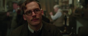 Movie still from “Their Finest” (2016), directed by Lone Scherfig – A person wearing glasses and a suit; Close Up shot, Over the shoulder angle