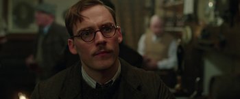 Movie still from “Their Finest” (2016), directed by Lone Scherfig – A man with a mustache and glasses is looking at the camera; Close Up shot, Over the shoulder angle