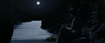 Movie still from “Their Finest” (2016), directed by Lone Scherfig – A woman sitting on the shore of a beach at night; Wide shot, High angle
