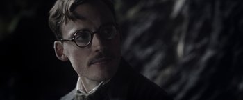 Movie still from “Their Finest” (2016), directed by Lone Scherfig – A person wearing glasses and a bow tie; Close Up shot, Over the shoulder angle
