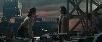 Movie still from “Their Finest” (2016), directed by Lone Scherfig – Two women standing next to each other on a dock; Medium shot, Over the shoulder angle