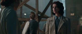 Movie still from “Their Finest” (2016), directed by Lone Scherfig – A man and a woman standing next to each other in front of a wooden structure; Medium shot, Over the shoulder angle