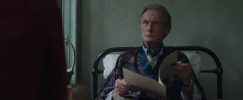 Movie still from “Their Finest” (2016), directed by Lone Scherfig – An older man sitting in a chair reading a paper; Medium shot, High angle