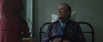 Movie still from “Their Finest” (2016), directed by Lone Scherfig – An older man sitting in a chair in a hospital room; Medium shot, High angle