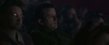 Movie still from “Their Finest” (2016), directed by Lone Scherfig – A man sitting in front of a group of people; Close Up shot, Low angle