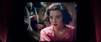 Movie still from “Their Finest” (2016), directed by Lone Scherfig – A young woman with red lipstick is sitting in front of a man holding a gun; Close Up shot, Over the shoulder angle