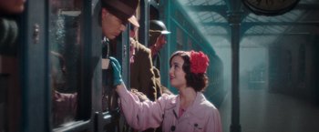 Movie still from “Their Finest” (2016), directed by Lone Scherfig – A woman in a pink coat is touching a man in a hat; Medium shot, Over the shoulder angle