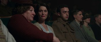 Movie still from “Their Finest” (2016), directed by Lone Scherfig – A group of people sitting next to each other in a room; Medium shot, Over the shoulder angle