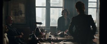 Movie still from “Their Finest” (2016), directed by Lone Scherfig – A woman sitting at a table in front of a window; Medium shot, Over the shoulder angle