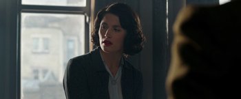 Movie still from “Their Finest” (2016), directed by Lone Scherfig – A woman in a black jacket and red lipstick; Close Up shot, Over the shoulder angle