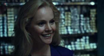 Movie still from “Thief” (1981), directed by Michael Mann – A woman smiling for the camera in front of a shelf; Close Up shot, Over the shoulder angle