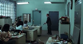 Movie still from “Thief” (1981), directed by Michael Mann – A man holding a gun in an office with people; Wide shot, High angle