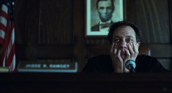 A man sitting at a desk in front of a picture of abraham lincoln