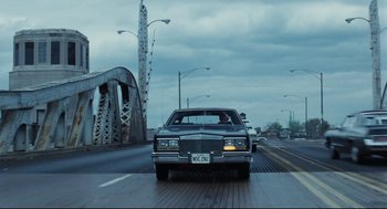 Movie still from “Thief” (1981), directed by Michael Mann – A car driving down a street next to a bridge; Wide shot, Low angle