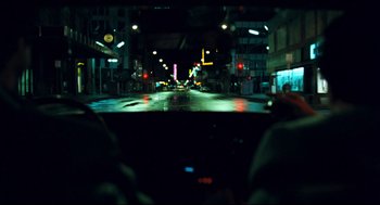 Movie still from “Thief” (1981), directed by Michael Mann – A view from a car of a street at night; Wide shot, Over the shoulder angle
