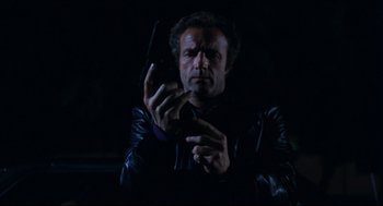 Movie still from “Thief” (1981), directed by Michael Mann – A man holding a cell phone while standing in the dark; Medium shot, Low angle