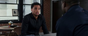 Movie still from “Think Like a Man” (2012), directed by Tim Story – A man sitting at a table in front of a brick wall; Close Up shot, Over the shoulder angle