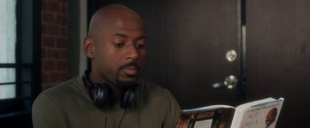 Movie still from “Think Like a Man” (2012), directed by Tim Story – A bald man with headphones is sitting in front of a book; Close Up shot, Over the shoulder angle