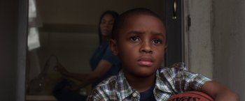 Movie still from “Think Like a Man” (2012), directed by Tim Story – A young boy is looking at the camera with a woman in the background; Close Up shot, High angle