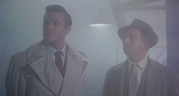 Movie still from “This Island Earth” (1955), directed by Joseph M. Newman – Two men in trench coats and a hat are standing in the fog; Medium shot, Low angle