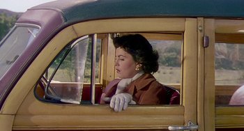 Movie still from “This Island Earth” (1955), directed by Joseph M. Newman – A woman sitting in the driver's seat of an old fashioned car; Medium shot, Over the shoulder angle