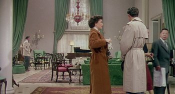 Movie still from “This Island Earth” (1955), directed by Joseph M. Newman – A woman in a trench coat standing next to a man in a trench coat in a living room; Wide shot, High angle