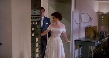 Movie still from “This Island Earth” (1955), directed by Joseph M. Newman – A man and a woman in formal wear standing in front of an electrical panel; Medium shot, Low angle