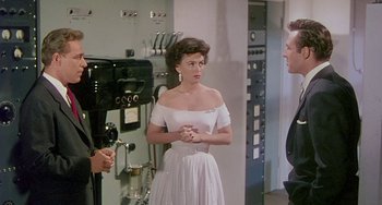 Movie still from “This Island Earth” (1955), directed by Joseph M. Newman – A woman in a white dress standing next to a man; Medium shot, Over the shoulder angle