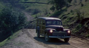 Movie still from “This Island Earth” (1955), directed by Joseph M. Newman – An old car driving down a dirt road near a forest; Wide shot, High angle