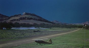 Movie still from “This Island Earth” (1955), directed by Joseph M. Newman – An airplane sitting on top of a grass covered field; Extreme Wide shot, Low angle